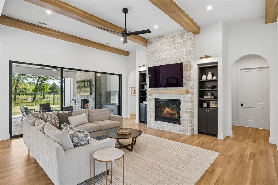 Spacious family room with a gas fireplace, custom shelving, beamed ceiling, and arched doorways.