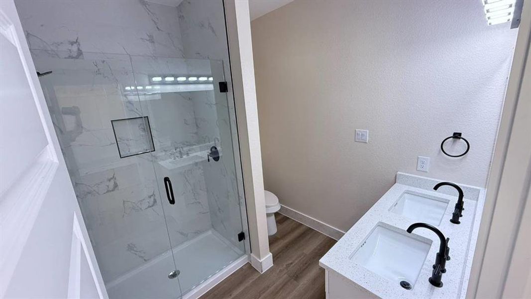 Bathroom with double vanity, a marble finish shower, and dark wood finished floors