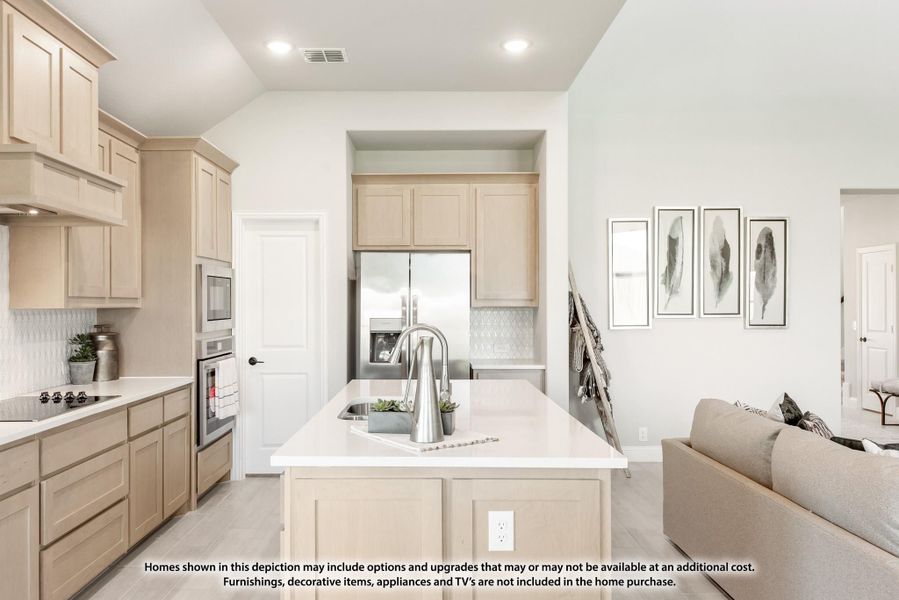 Open kitchen with light wood cabinets, center island with sink, and stainless steel appliances open to living area