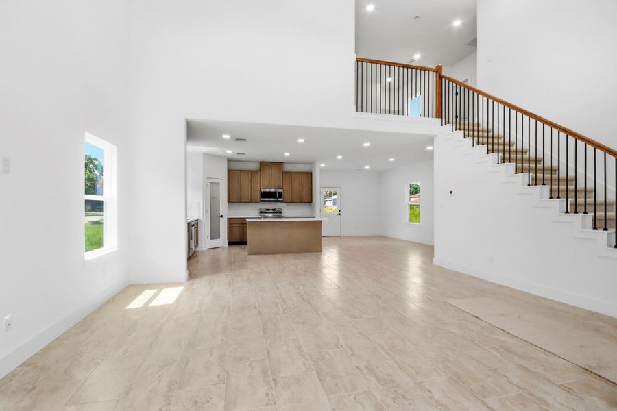 Spacious open-concept living area features high ceilings, a sleek kitchen with modern appliances, and an elegant staircase leading to the upper level.