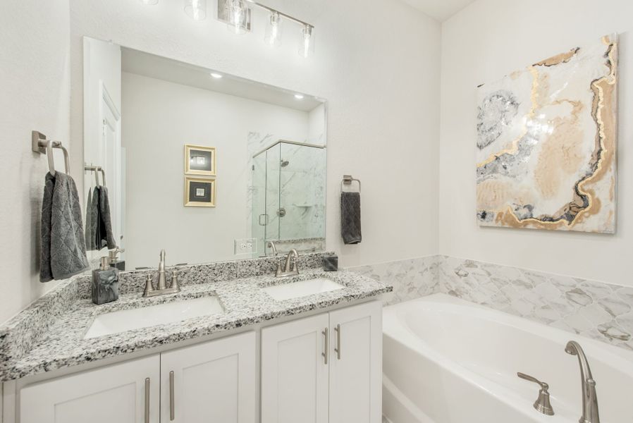 Bathroom with double granite vanity, soaking tub with marble surround, and glass shower enclosure