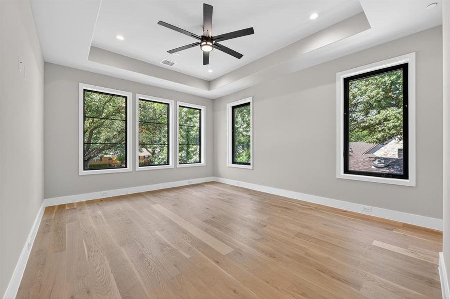 Spacious room featuring light wood-finish flooring, a tray ceiling with recessed lighting, and a modern ceiling fan Spacious room featuring light wood-finish flooring, a tray ceiling with recessed lighting, and a modern ceiling fan
