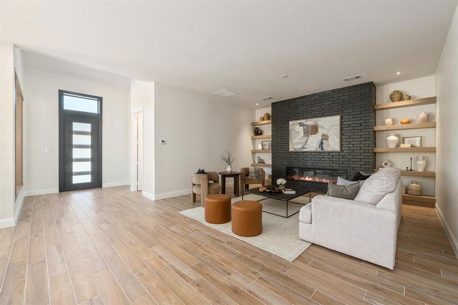 Living area featuring built in shelves, a brick fireplace, and light wood finished floors Living area featuring built in shelves, a brick fireplace, and light wood finished floors