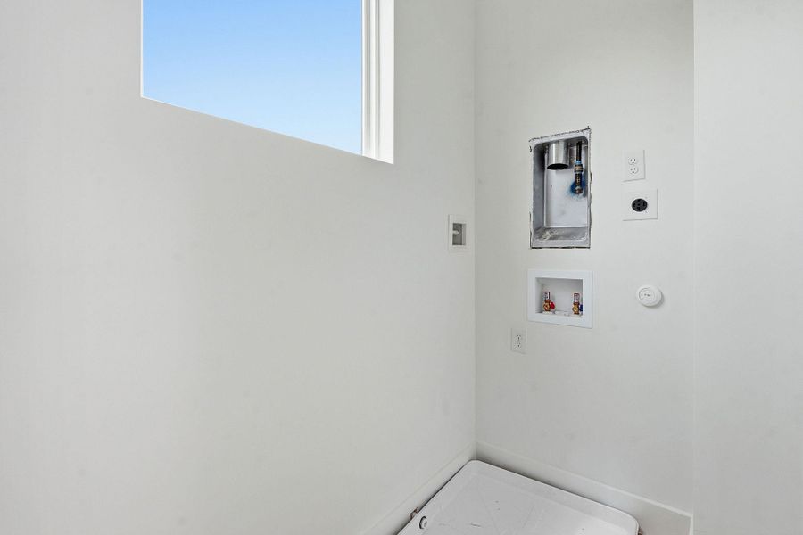 Dedicated laundry area featuring a high window, white walls, and comprehensive hookups including electrical outlets and water connections