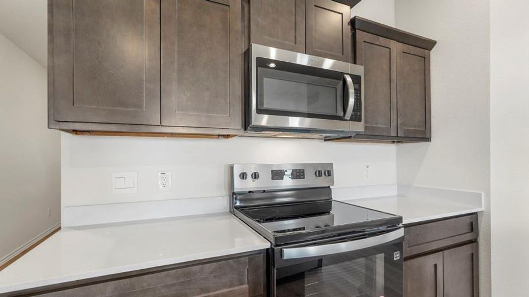 Kitchen featuring gray shaker-style cabinetry, a stainless steel electric range, an over-the-range microwave, and light-toned countertops