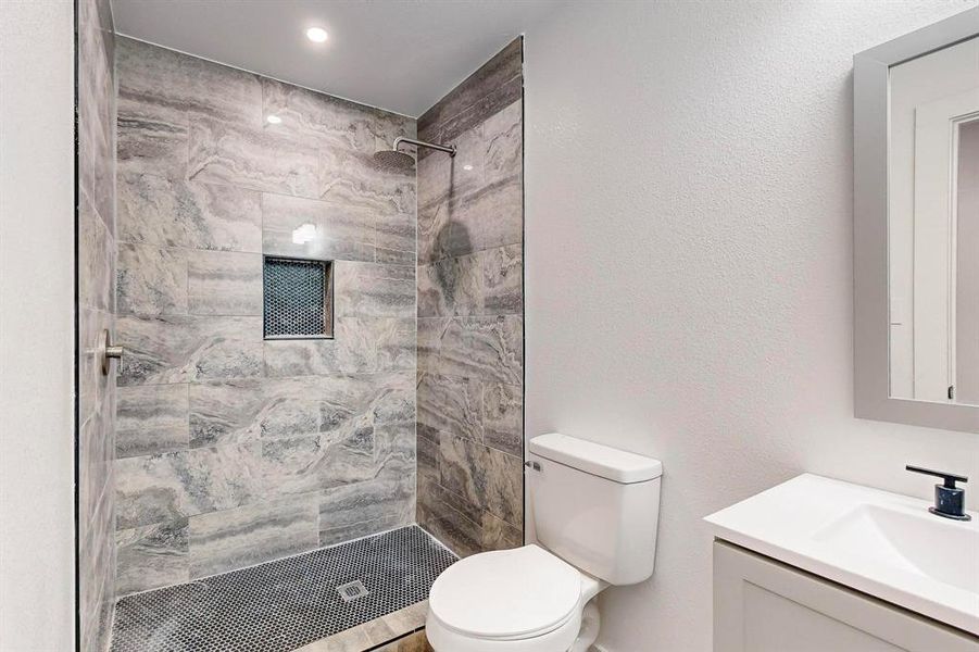 Bathroom featuring vanity, toilet, and a tile shower