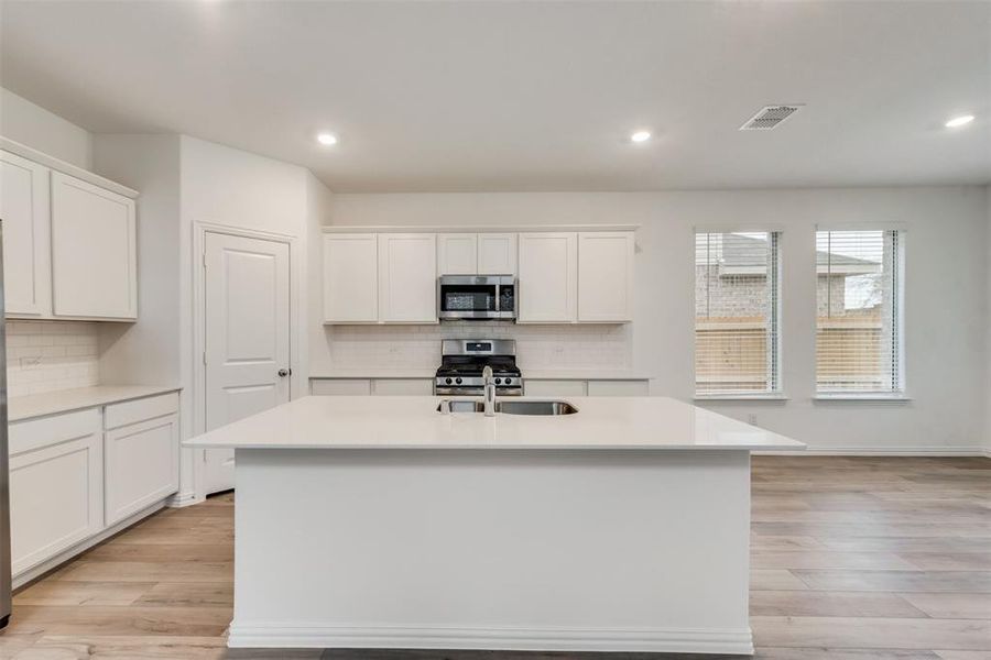 Kitchen featuring a center island with sink, light hardwood / wood-style flooring, stainless steel appliances, and backsplash