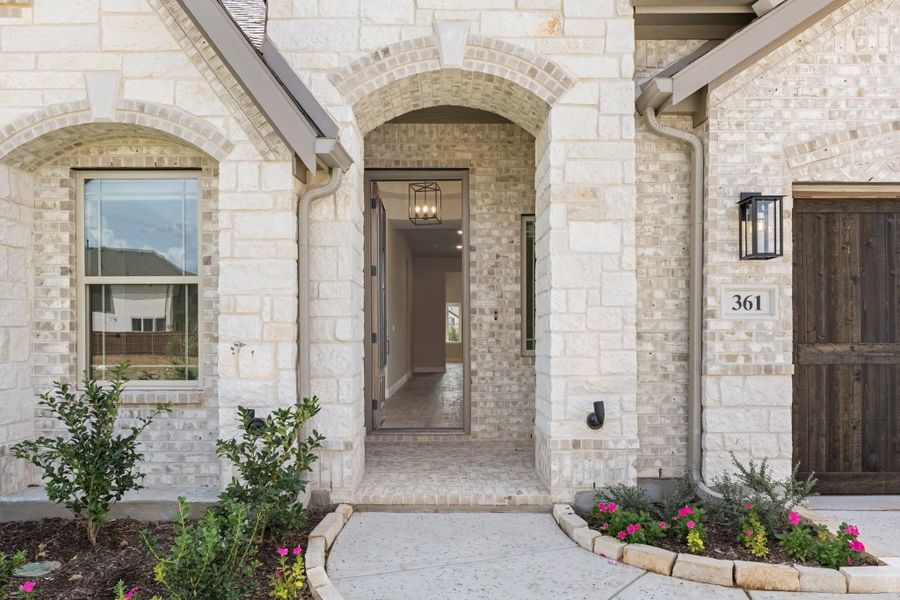 Stone home exterior with arched entryway, open front door, and landscaped walkway leading inside Stone home exterior with arched entryway, open front door, and landscaped walkway leading inside
