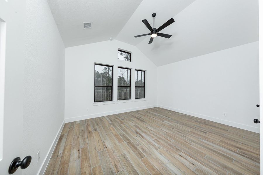 Relax and unwind after a long day in this impressive primary suite! This generously sized room offers the same wood look tile flooring, neutral-toned paint, cathedral ceilings with a ceiling fan, and large windows for added comfort and tranquility.