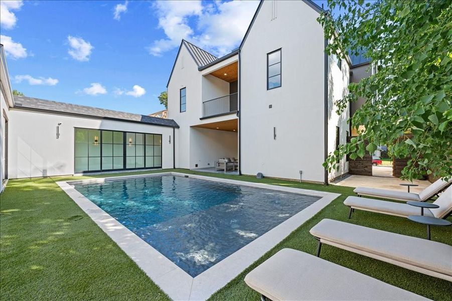 Rear view of property with an outdoor pool, a patio, a lawn, and a standing seam roof