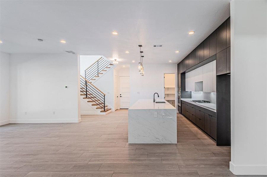 Kitchen with modern cabinets, a center island with sink, recessed lighting, hanging light fixtures, and light stone counters