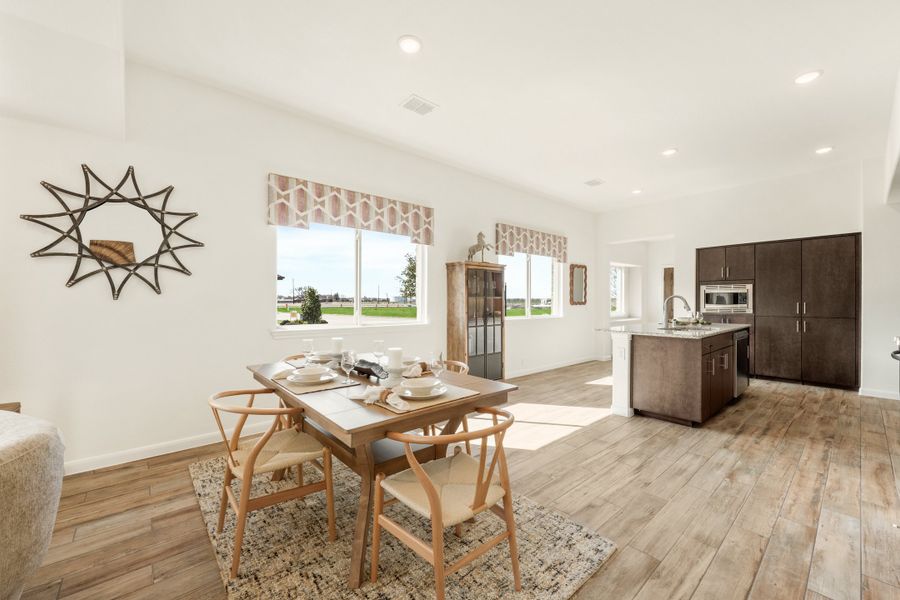 Open dining area with wood table and chairs, flowing into kitchen with dark cabinets and hardwood floors