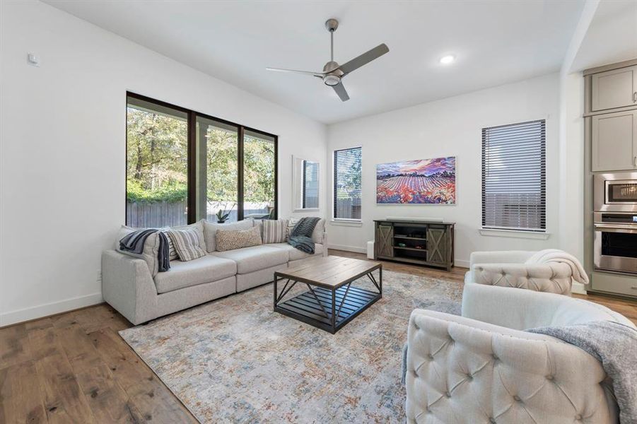 The family room is warm and inviting, featuring a modern ceiling fan and an abundance of windows that flood the space with natural light, creating a cozy atmosphere for relaxation and gatherings.