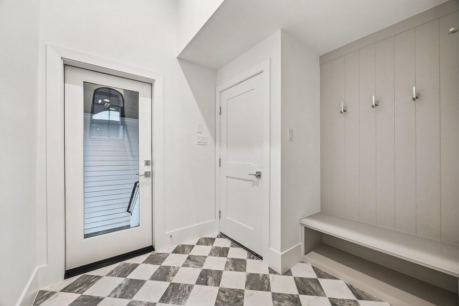 MUD Area off of the garage and the back patio with a 24 x 24 Checkerboard Matte Porcelain Tile in Calcutta and Amani Grey. There is also a built-in bench and hooks.