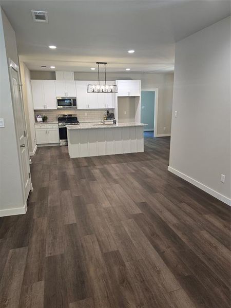 Kitchen with hanging light fixtures, range, an island with sink, white cabinets, and dark hardwood / wood-style floors