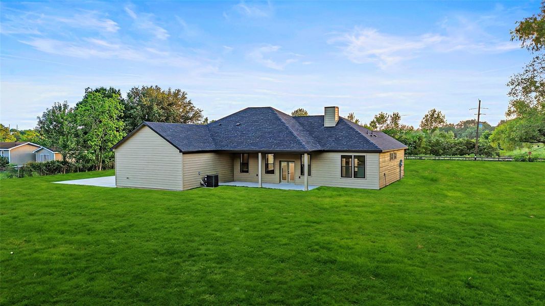 This photo showcases a single-story home with a spacious backyard, and a covered patio area. This photo showcases a single-story home with a spacious backyard, and a covered patio area.