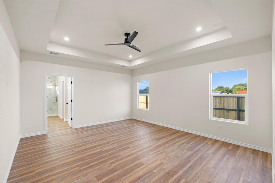 Empty room with light wood-style floors, a tray ceiling, a ceiling fan, and recessed lighting Empty room with light wood-style floors, a tray ceiling, a ceiling fan, and recessed lighting