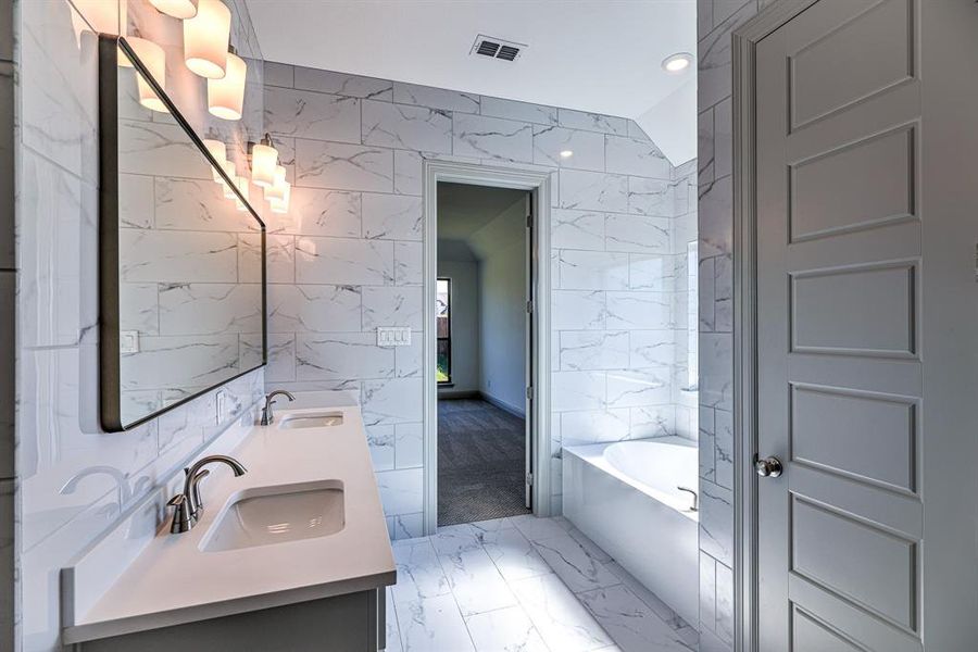 Bathroom featuring tile walls, double vanity, a tub to relax in, light marble finish floors, and recessed lighting Bathroom featuring tile walls, double vanity, a tub to relax in, light marble finish floors, and recessed lighting