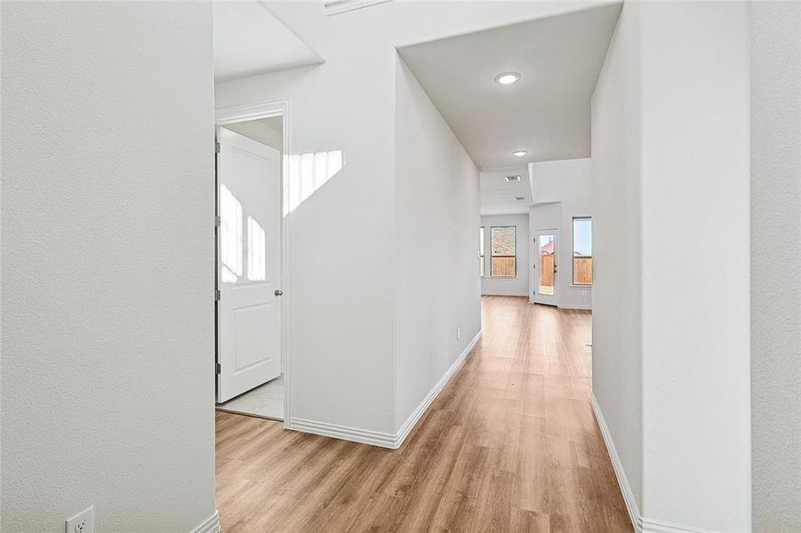 Hallway featuring light wood-style floors, a textured wall, and recessed lighting