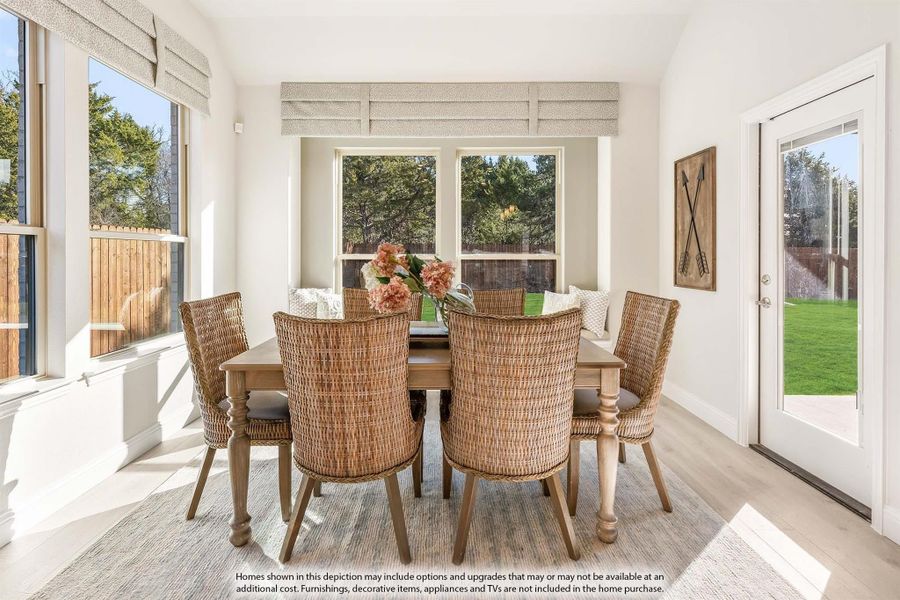 Bright dining area with wood table, wicker chairs, bench seating, and large windows overlooking a backyard