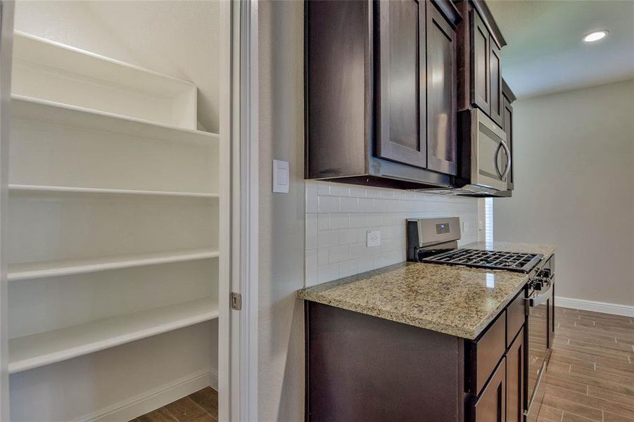 Kitchen with stainless steel appliances, dark brown cabinetry, tasteful backsplash, light wood-style flooring, and light stone counters Kitchen with stainless steel appliances, dark brown cabinetry, tasteful backsplash, light wood-style flooring, and light stone counters
