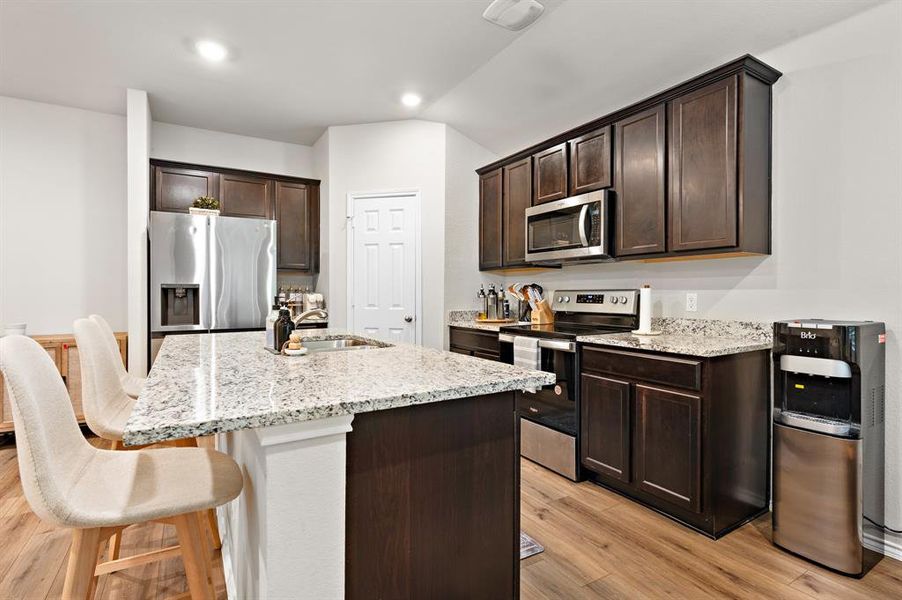 Kitchen featuring dark brown cabinets, stainless steel appliances, and light stone counters Kitchen featuring dark brown cabinets, stainless steel appliances, and light stone counters