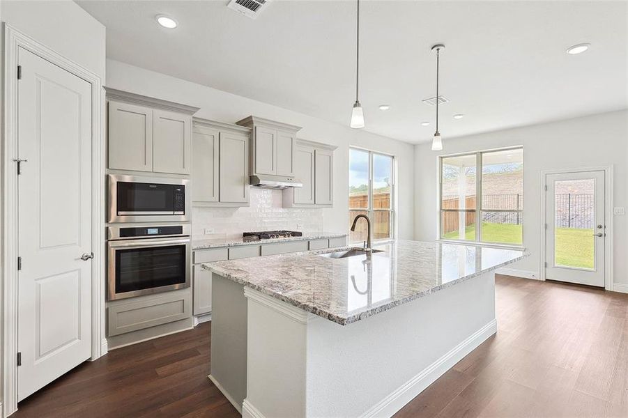 Kitchen with stainless steel appliances, a center island with sink, sink, decorative backsplash, and dark wood-type flooring