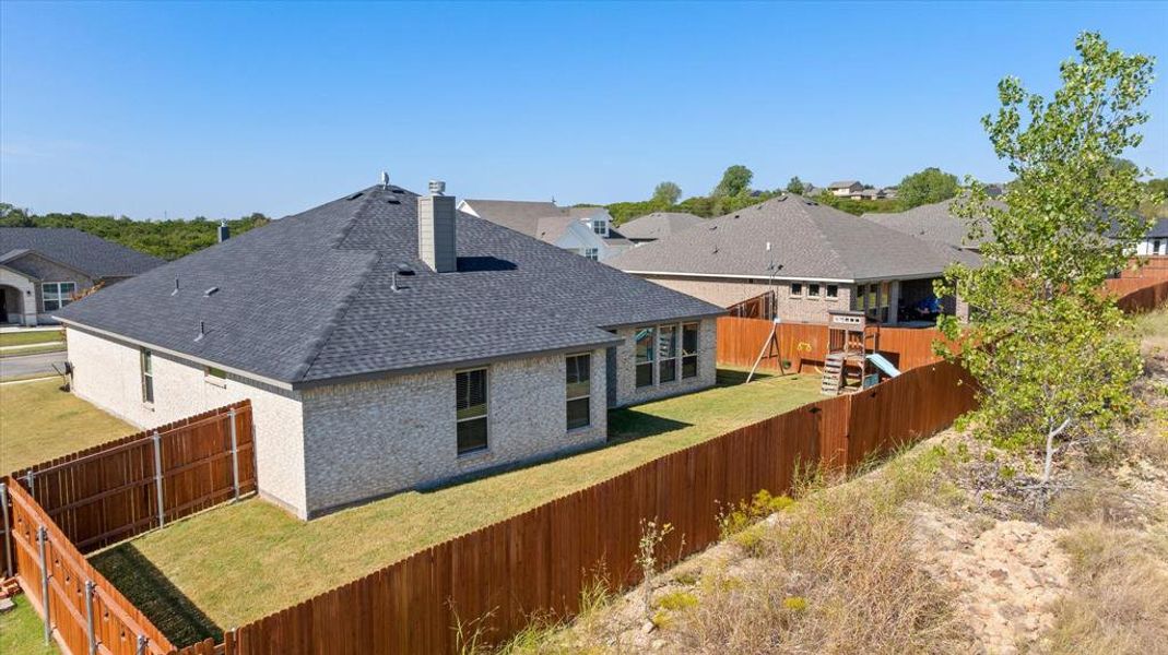 Back of house featuring a fenced backyard, a chimney, brick siding, a residential view, and roof with shingles
