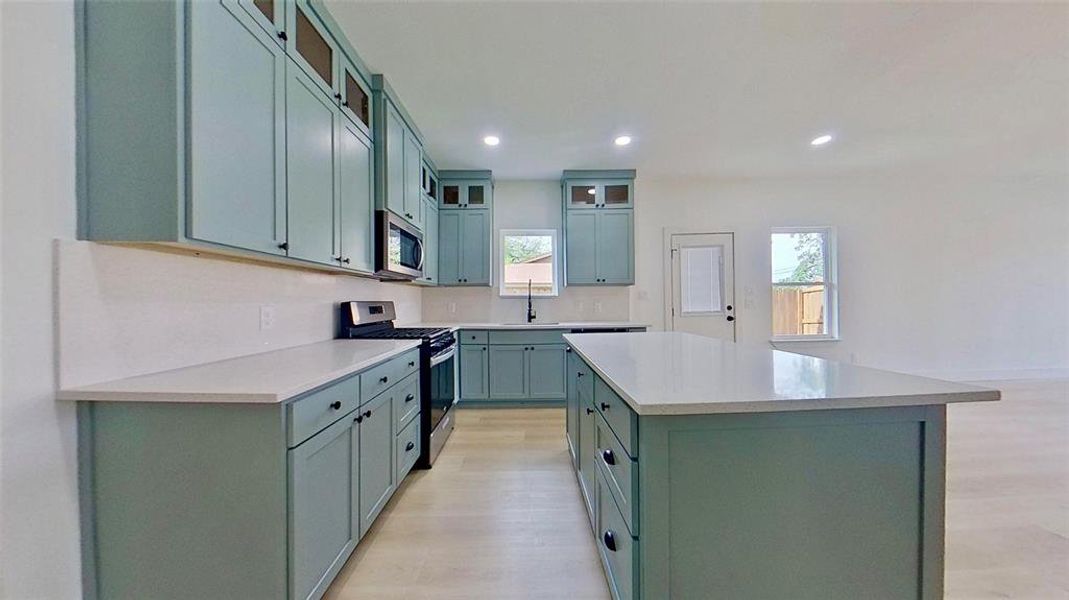 Kitchen featuring light blue cabinetry, light-toned countertops, a central island, stainless steel appliances, and wood-finish flooring