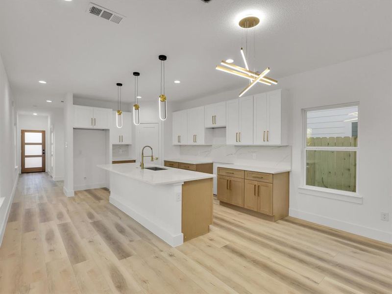 Kitchen with light wood-type flooring, a center island with sink, white cabinetry, and hanging light fixtures