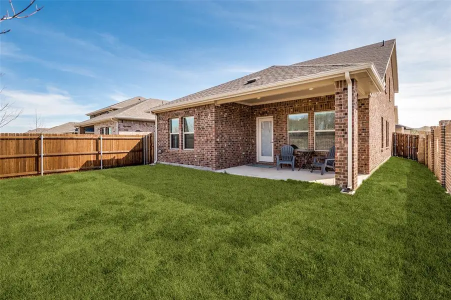 Rear view of house featuring brick siding, a fenced backyard, a patio area, and roof with shingles