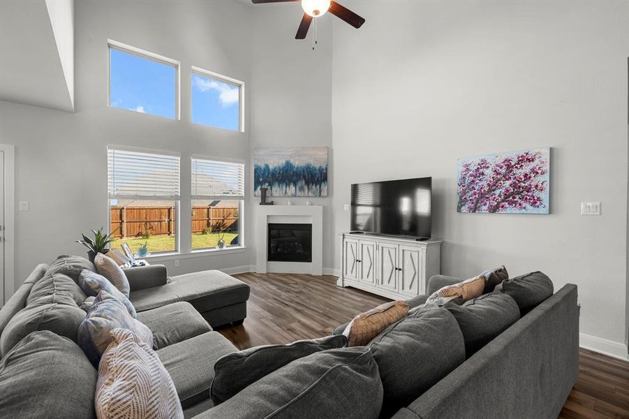 Living room with a high ceiling, a fireplace, wood finished floors, and a ceiling fan Living room with a high ceiling, a fireplace, wood finished floors, and a ceiling fan