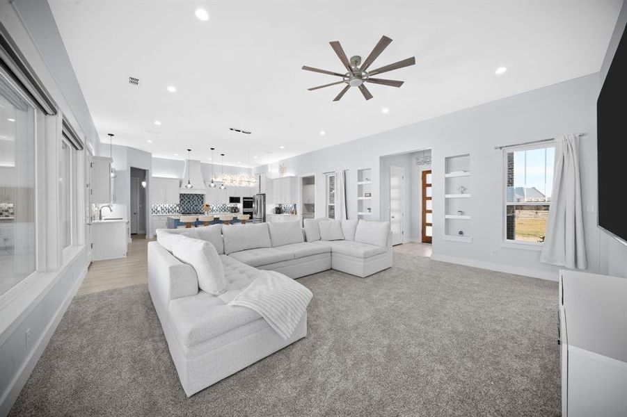 Living area featuring built in shelves, light colored carpet, ceiling fan, and recessed lighting