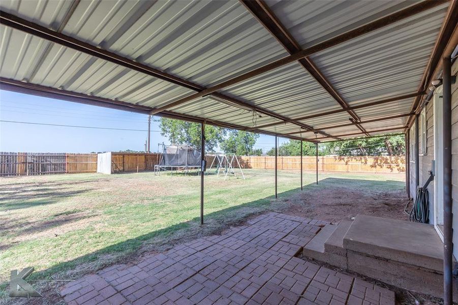 Fenced backyard featuring a trampoline, a patio area, and a playground