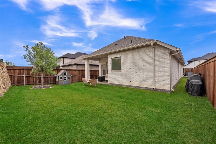Expansive backyard featuring a manicured lawn, a mature tree, and a covered patio area Expansive backyard featuring a manicured lawn, a mature tree, and a covered patio area