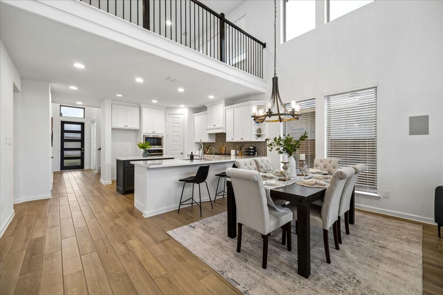 The dining area rests beautifully between the island kitchen and open family room, creating an easy flow for meals, gatherings, and everyday connection. Soaring 19’ ceilings, soft natural light, and wood-look tile flooring make the heart of the home feel bright, spacious, and welcoming.