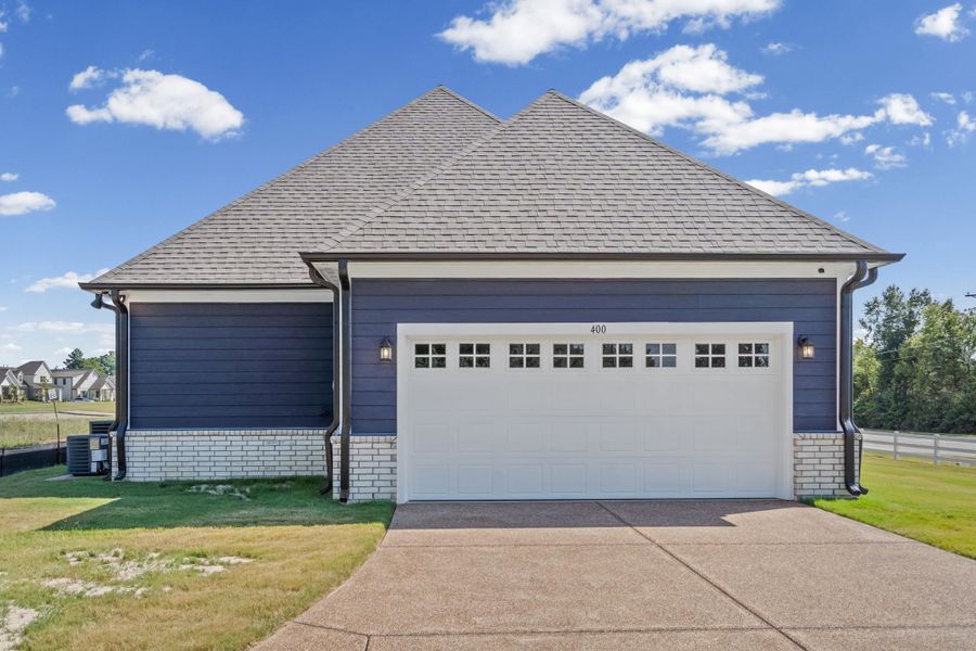 Siding exterior with a light-colored brick foundation, a pitched roof, and an attached two-car garage with transom-style windows