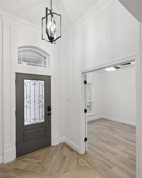 Foyer with a towering ceiling, a notable chandelier, crown molding, and light wood-type flooring