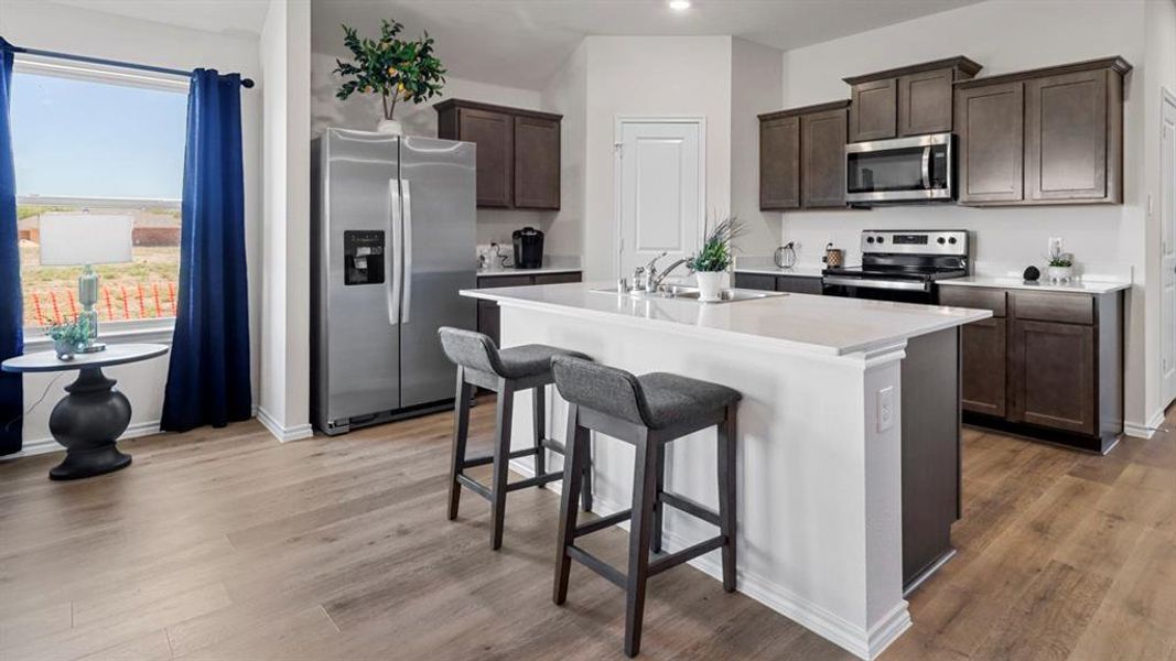 Kitchen featuring stainless steel appliances, dark wood finish cabinets, a kitchen breakfast bar, a center island with sink, and dark wood-style flooring