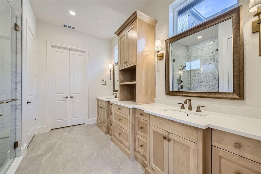 Primary bathroom with custom double vanity with storage, framed mirrors, a frameless glass shower and a transom window.