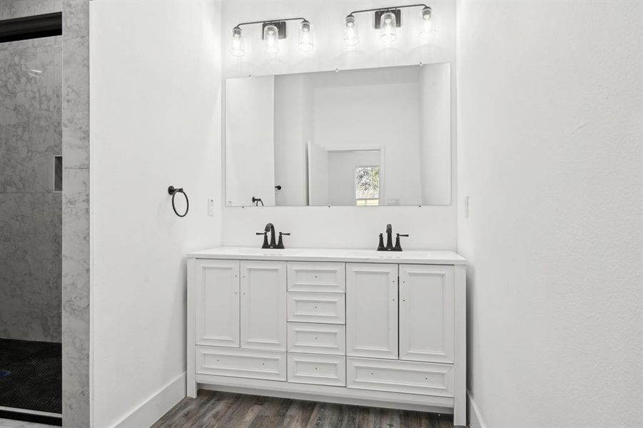 Bathroom with double vanity, a sink, wood finished floors, tiled shower, and baseboards