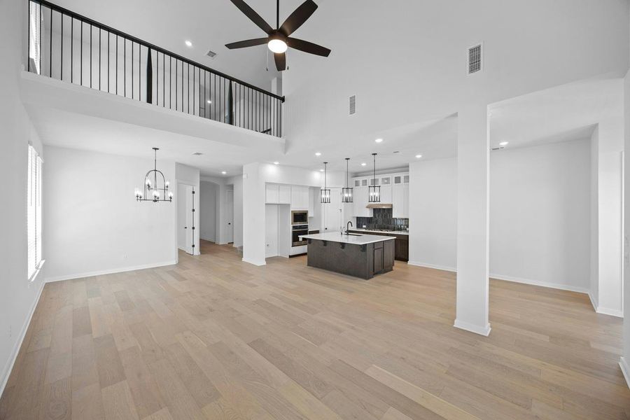 Unfurnished living room with ceiling fan, a high ceiling, light wood-type flooring, a chandelier, and recessed lighting Unfurnished living room with ceiling fan, a high ceiling, light wood-type flooring, a chandelier, and recessed lighting
