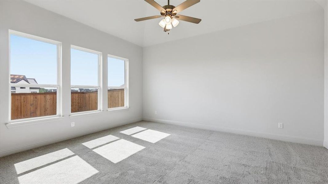 Bright interior room featuring a vaulted ceiling, three large windows, a ceiling fan with integrated lighting, and neutral carpeting
