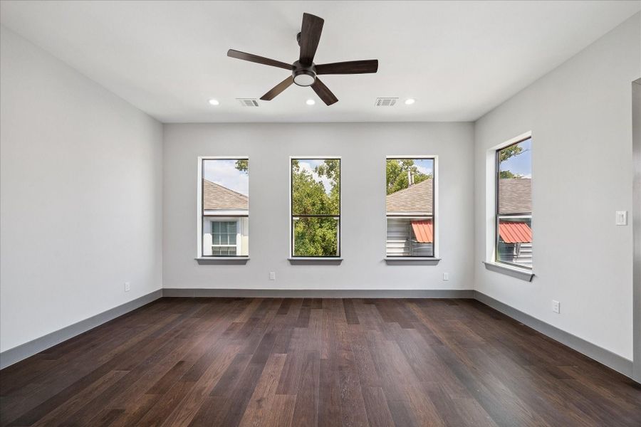 Generous natural light streams through four tall windows, highlighting the warm wood floors and neutral palette. Ample square footage offers flexibility for large furniture, a sitting area, or even a home office corner.