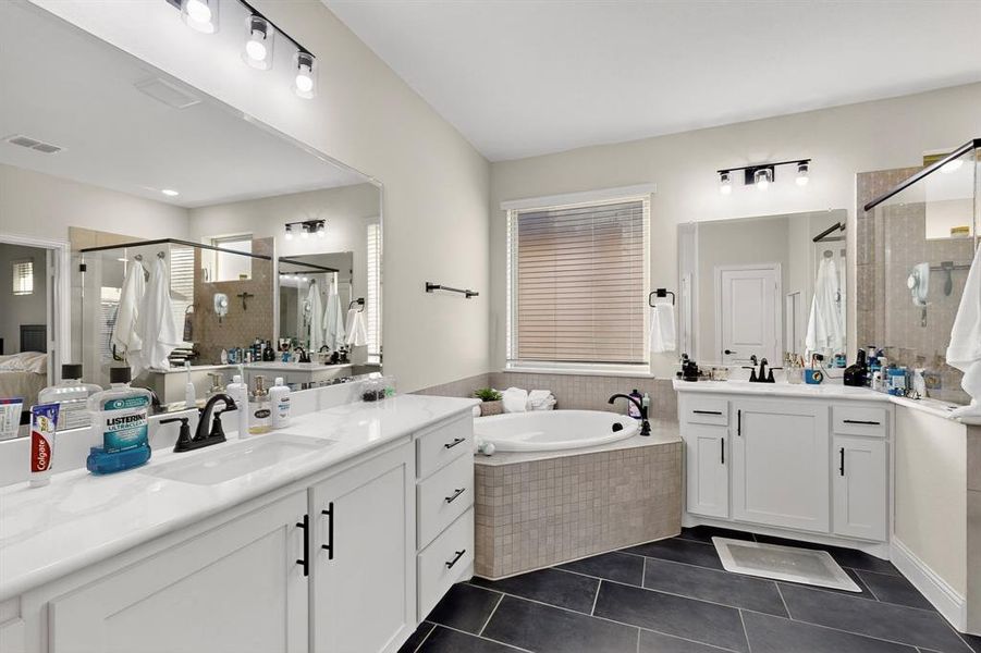Full bath with two vanities, dark tile patterned flooring, a shower stall, and a garden tub Full bath with two vanities, dark tile patterned flooring, a shower stall, and a garden tub