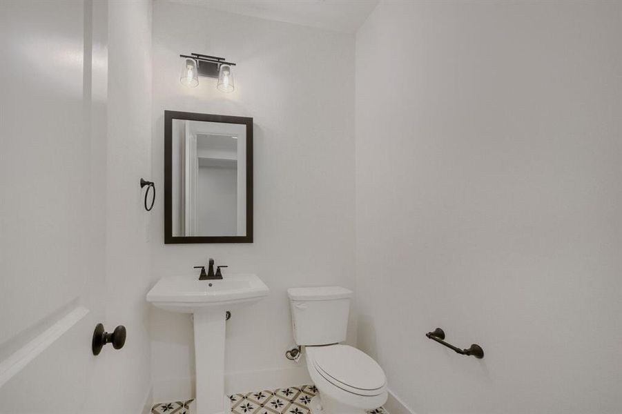 Pedestal sink with a black-framed rectangular mirror, black wall-mounted light fixture, and patterned floor tile