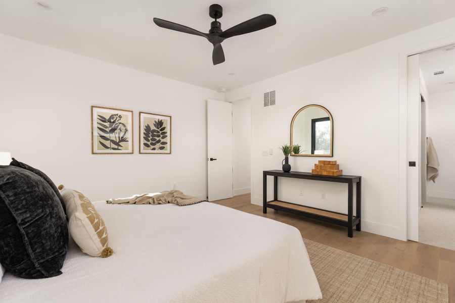 Hardwood floors and a subtle rug enhance this bright bedroom, complete with a modern ceiling fan and an adjacent en-suite or closet.