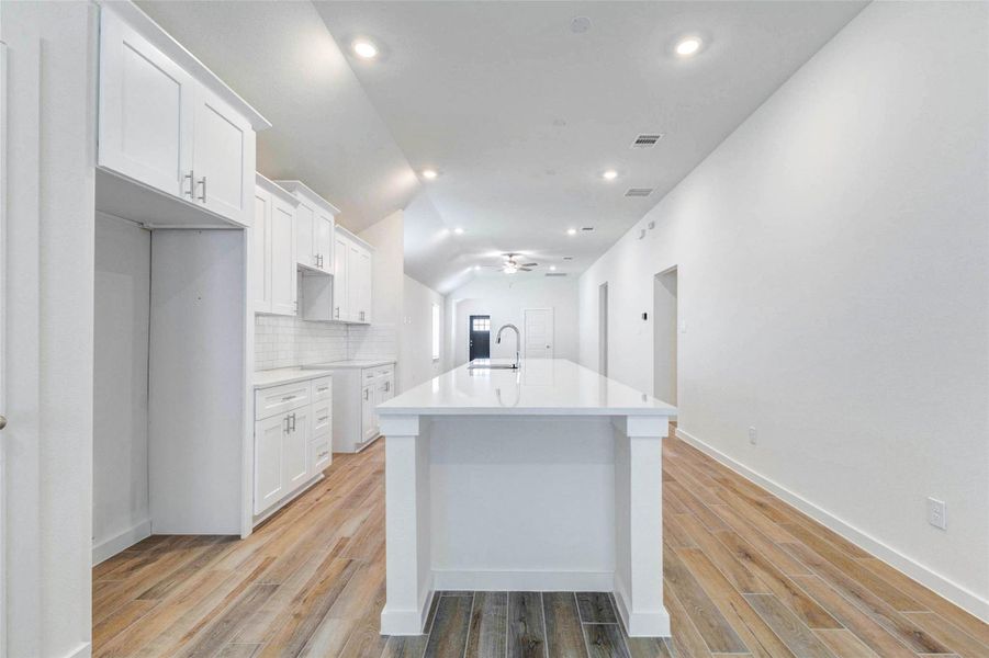 This kitchen view showcases the oversized island, white cabinetry, recessed lighting, and long, open layout. The wood-look tile adds warmth while the clean white finishes keep the space bright and modern. With easy connection to the living area, this kitchen is designed for everyday comfort and entertaining. This kitchen view showcases the oversized island, white cabinetry, recessed lighting, and long, open layout. The wood-look tile adds warmth while the clean white finishes keep the space bright and modern. With easy connection to the living area, this kitchen is designed for everyday comfort and entertaining.