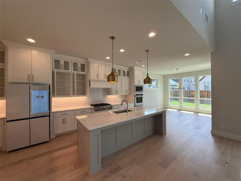 Kitchen with stainless steel appliances, decorative backsplash, glass insert cabinets, recessed lighting, and decorative light fixtures Kitchen with stainless steel appliances, decorative backsplash, glass insert cabinets, recessed lighting, and decorative light fixtures