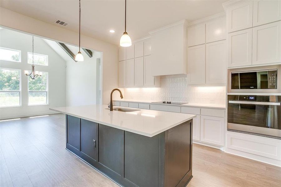 Kitchen featuring an island with sink, oven, sink, light hardwood / wood-style flooring, and backsplash